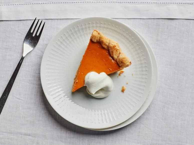 A slice of pumpkin pie with a dollop of whipped cream on a white plate.